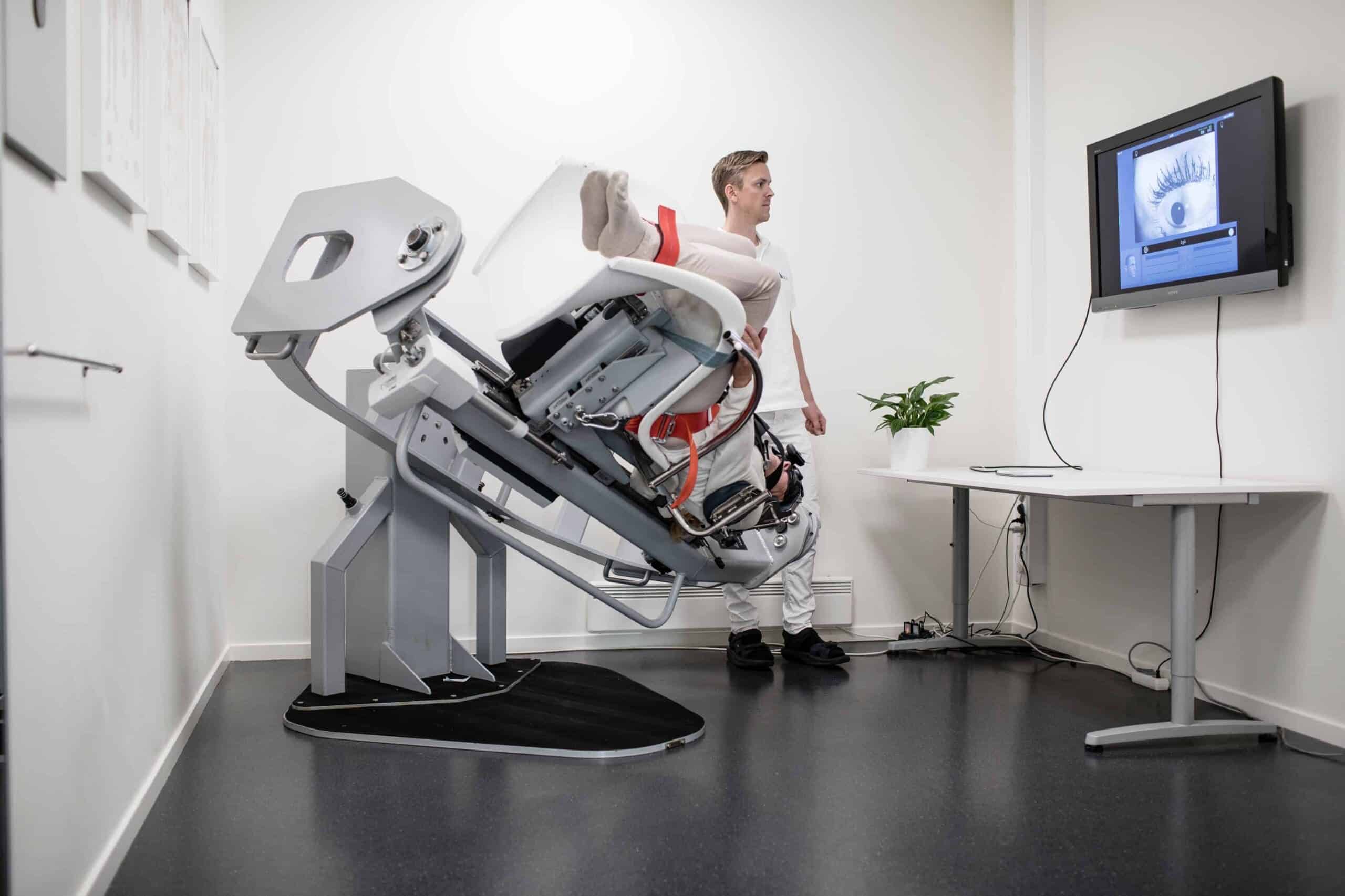 Patient i TRV-stol vid yrselutredning, med skärm i klinikrummet.