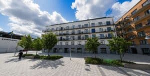 Modern flerbostadshus i Haninge med träd och sittplatser framför.