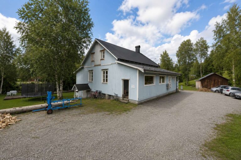 Lantligt hus med grön omgivning och blå himmel.