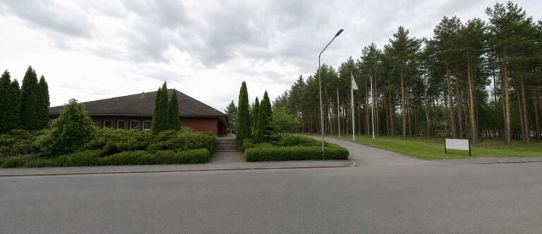 Landskapsbild av en byggnad omgiven av träd och buskar i Katrineholm.
