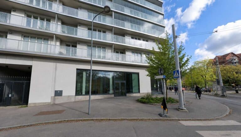 Modern byggnad vid Liljeholmen med träd och gångväg.