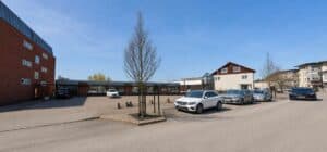 Parkering framför en skolbyggnad i Tingsryd på en solig dag.