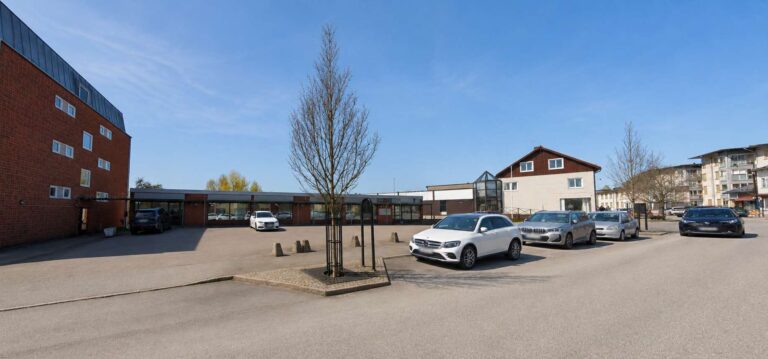 Parkering framför en skolbyggnad i Tingsryd på en solig dag.