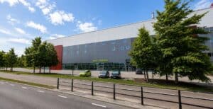 Modern wellnesscenter i Växjö med gröna träd och parkeringsplatser.