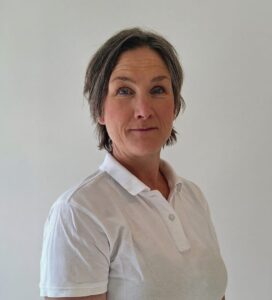 Kvinna med kort, grått hår i vit polo mot en ljus bakgrund.
