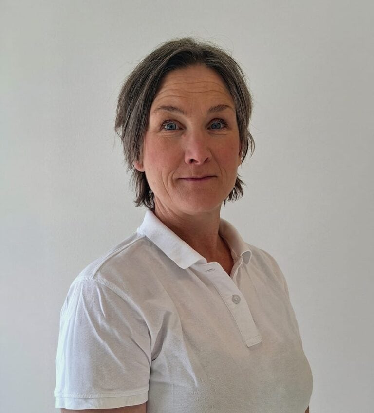 Kvinna med kort, grått hår i vit polo mot en ljus bakgrund.