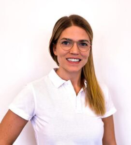 Kvinna med glasögon och vitt polo mot vit bakgrund.