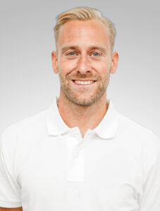 Man i vit polo shirt med ljus bakgrund, leende.