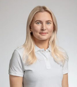 Kvinna med blont hår och vit polo mot ljus bakgrund.