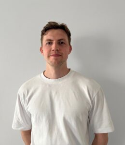 Man i vit t-shirt står framför en ljusgrå vägg.