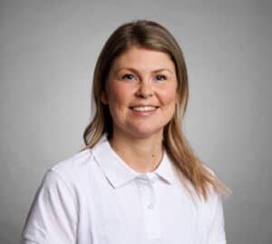 Kvinna med ljusbrunt hår och vit skjorta ler mot kameran.