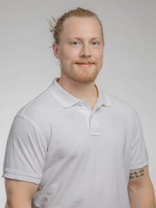 Ung man med blont hår och skägg i vit polo-shirt.
