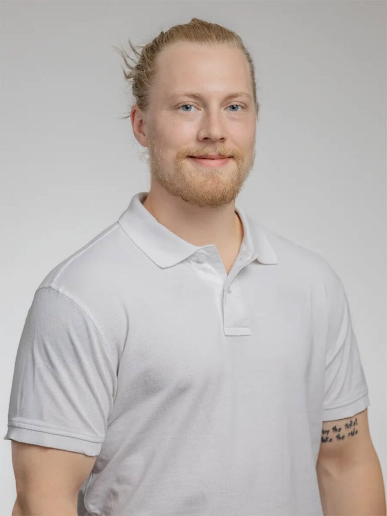 Ung man med blont hår och skägg i vit polo-shirt.