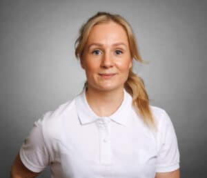 Porträtt av en kvinna i vit polo mot grå bakgrund.