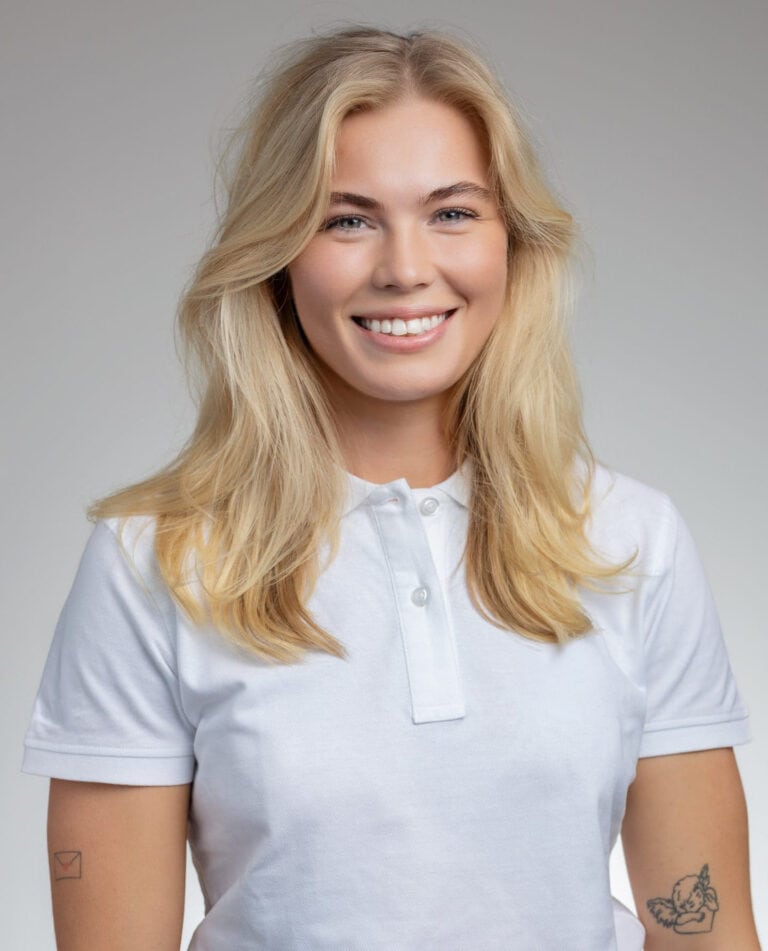 Ung kvinna med blont hår och vit polo, ler mot kameran.