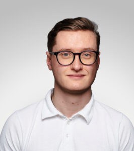 Ung man med glasögon och vit skjorta mot ljus bakgrund.