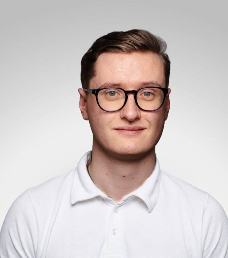 Ung man med glasögon och vit skjorta mot ljus bakgrund.