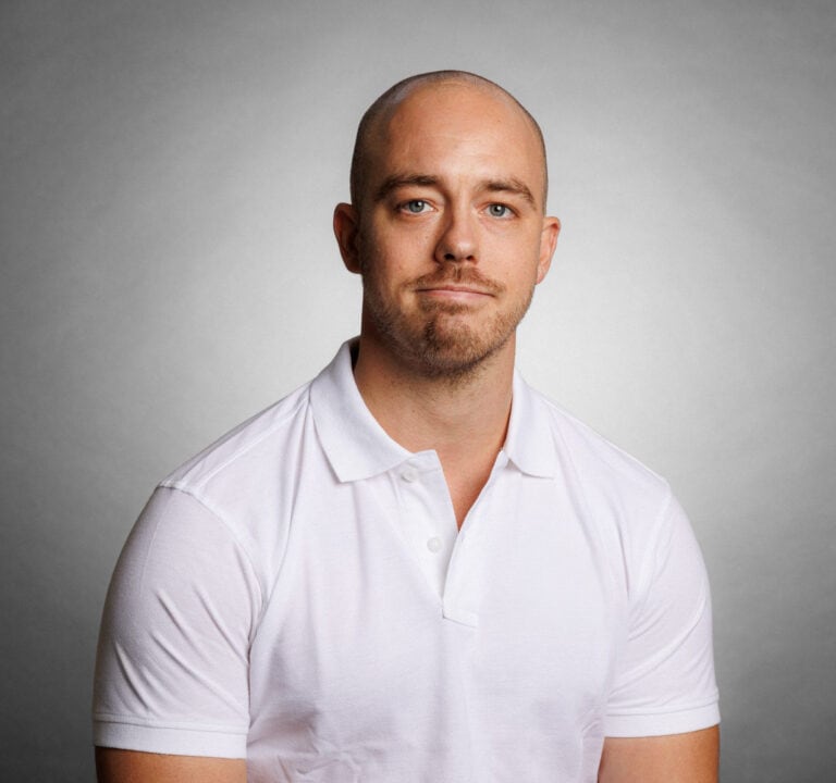 Porträtt av en man i vit polo mot grå bakgrund.