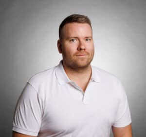 Porträtt av Jimmie Sjögren i vit polo mot grå bakgrund.