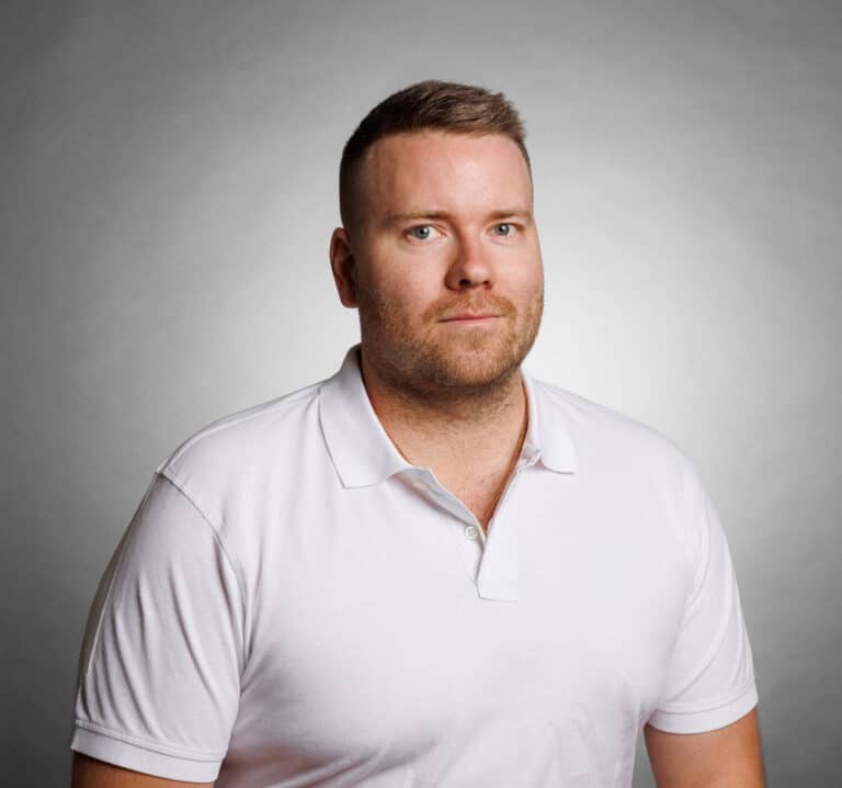 Porträtt av Jimmie Sjögren i vit polo mot grå bakgrund.