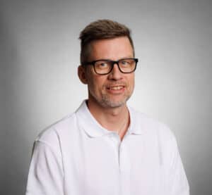 Man with glasses and white shirt smiling at camera.