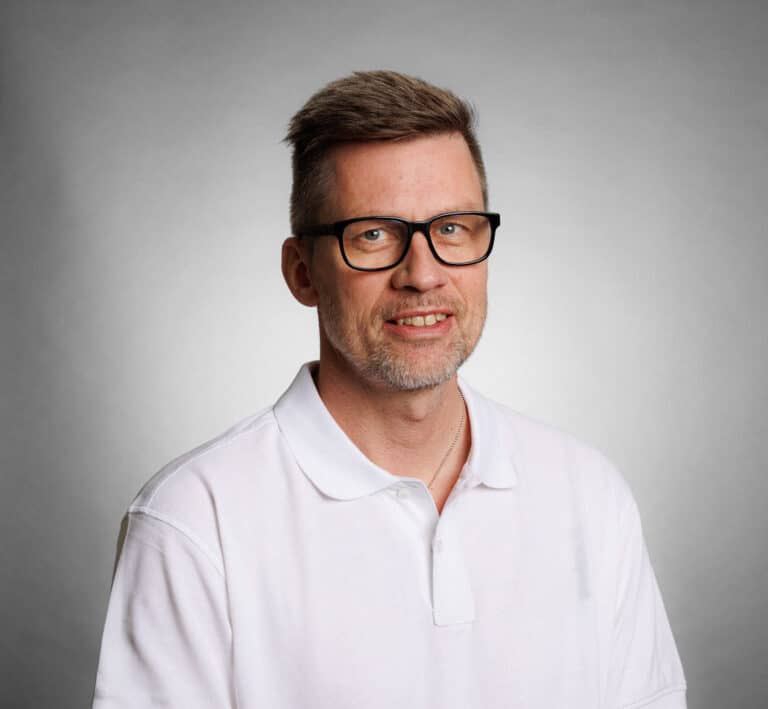 Man with glasses and white shirt smiling at camera.