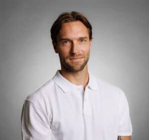 Man i vit polo shirt mot grå bakgrund.
