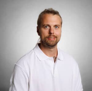 Porträtt av Joel Enlund i vit skjorta mot ljusgrå bakgrund.