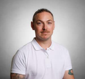 Porträtt av Johan Fjärrfors i vit polo mot grå bakgrund.