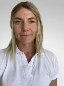 Kvinna med blont hår och vit polo mot ljus bakgrund.