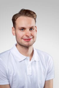 Ung man i vit skjorta med lätt leende mot kameran.