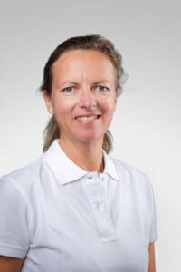 Kvinna i vit polo mot ljusgrå bakgrund.