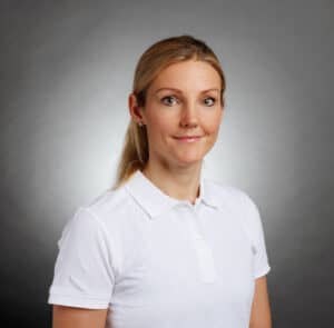 Kvinna i vit polo mot grå bakgrund.