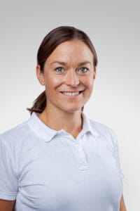 Kvinna med brunt hår och vit polo, ler mot kameran.