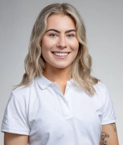 Glad kvinna med blont, vågigt hår i vit polo mot ljusgrå bakgrund.