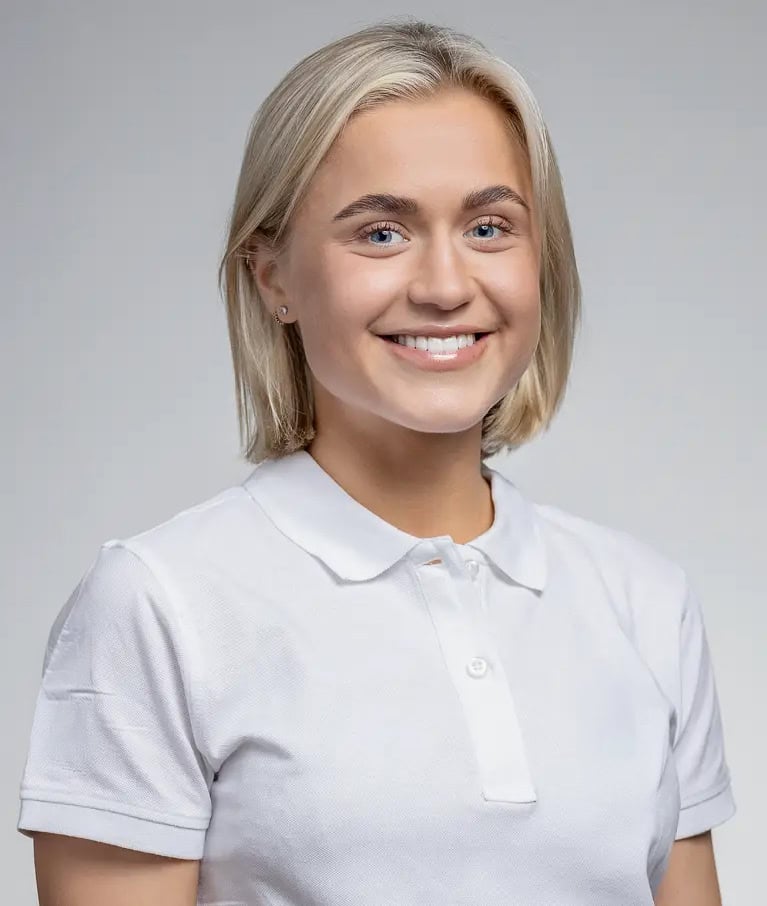 Ung kvinna med blont hår och vit polo, ler mot kameran.