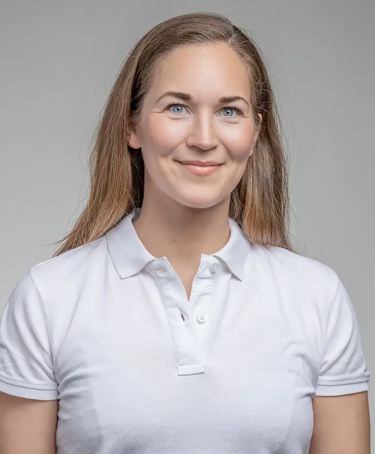 Kvinna med ljusbrunt hår i vit polo mot grå bakgrund.