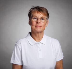 Kvinna i vit polo mot grå bakgrund.