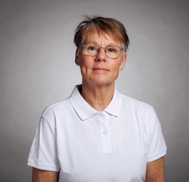 Kvinna i vit polo mot grå bakgrund.