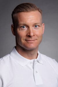 Porträtt av Pär Magnusson i vit skjorta mot grå bakgrund.
