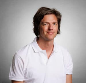 Man i vit polo shirt mot ljusgrå bakgrund.