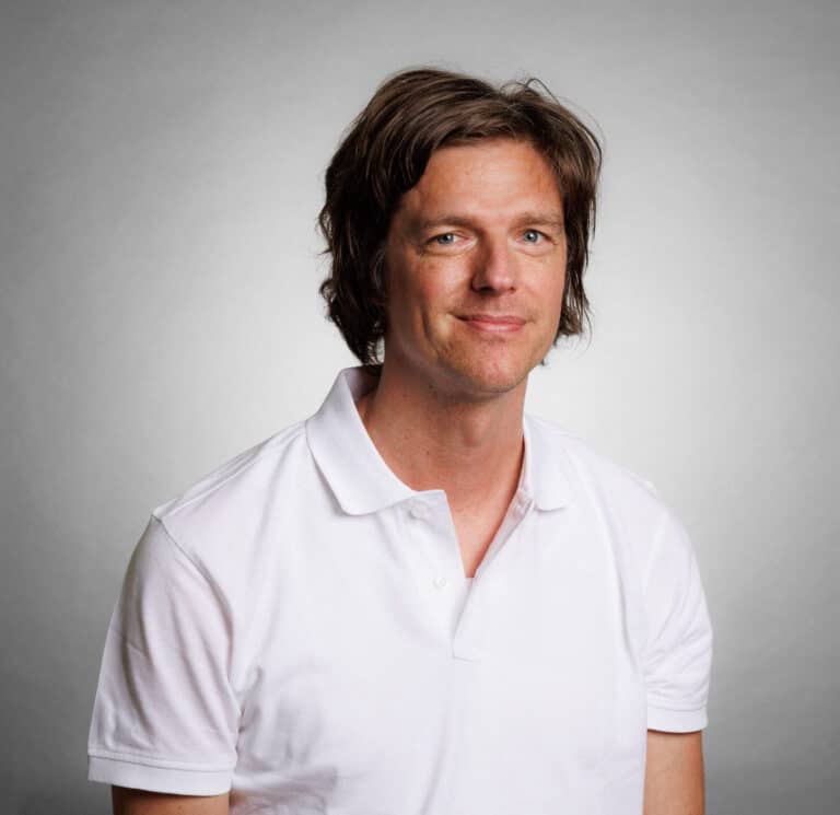 Man i vit polo shirt mot ljusgrå bakgrund.
