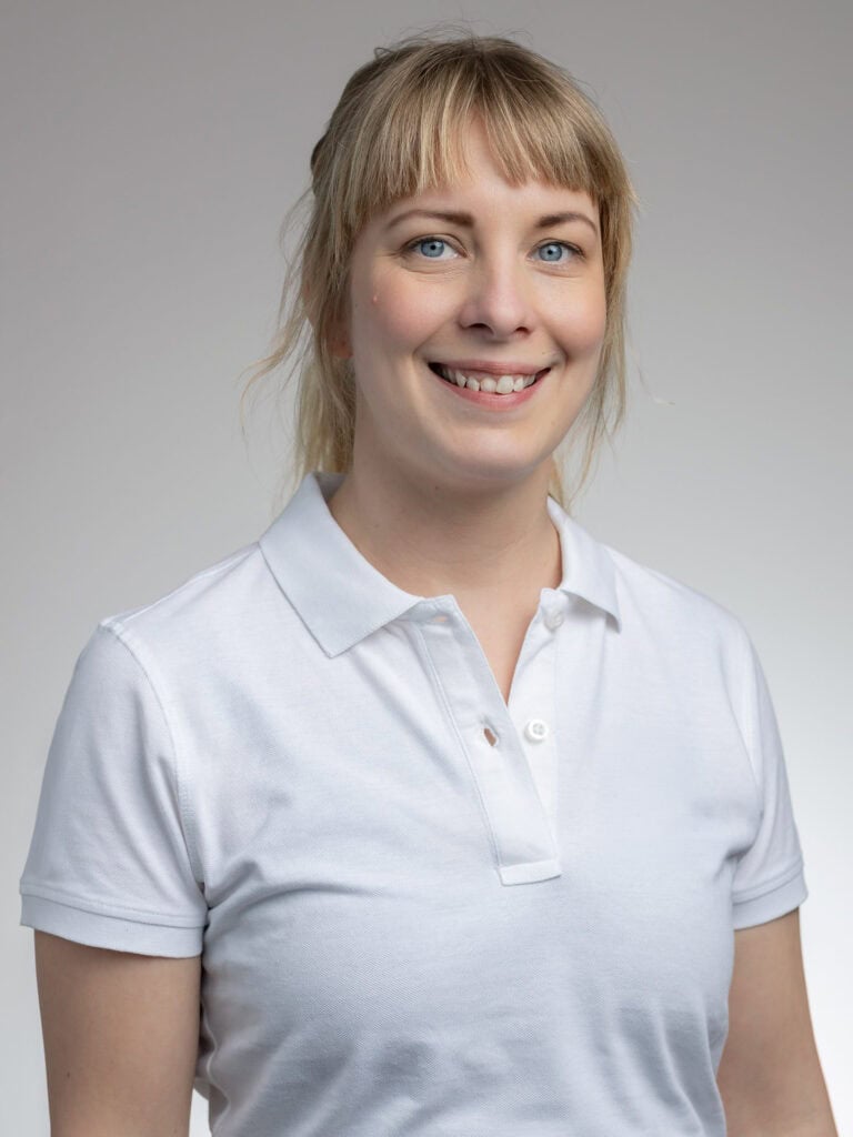 Kvinna med blont hår och vitt polo, ler mot kameran.