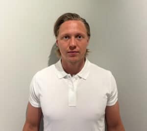Man i vit polo tröja står mot vit vägg.