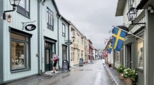 Kullerstensgata i Sigtuna med trähus, skyltfönster och svensk flagga.