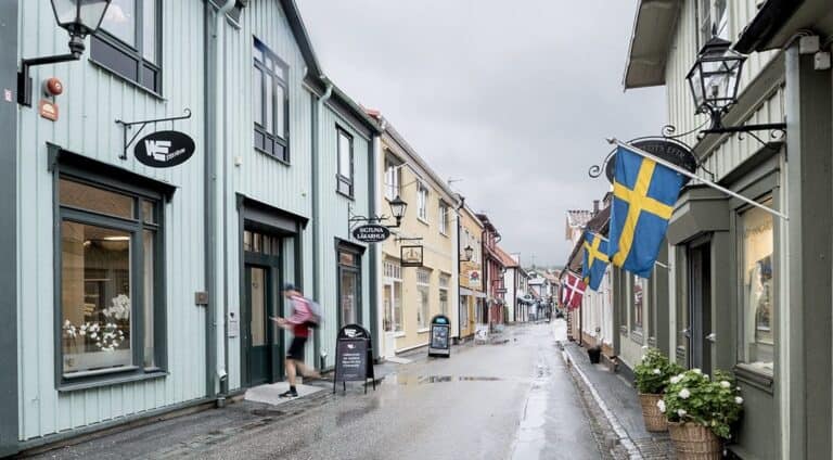 Kullerstensgata i Sigtuna med trähus, skyltfönster och svensk flagga.