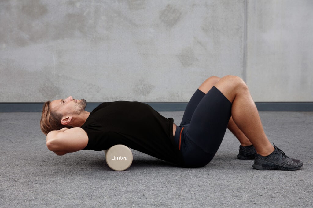 Man gör ryggövning med foam roller bakom huvudet.