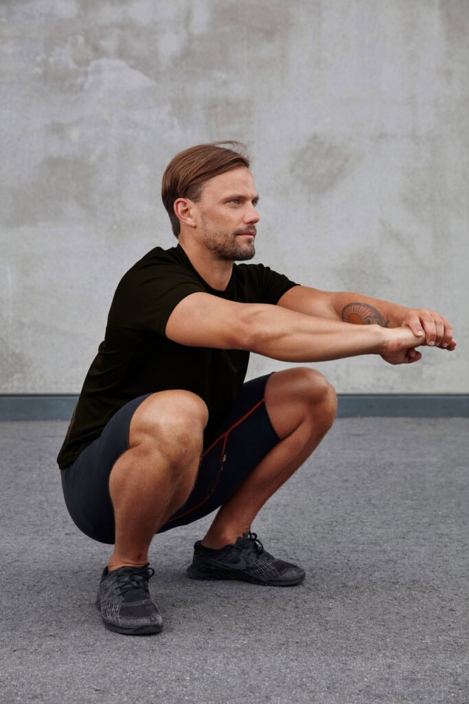 Man performing squat stretch for leg and core strength.