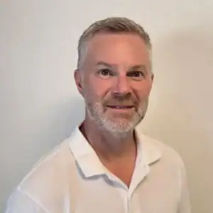 Porträtt av Michael Sandberg i vit skjorta mot ljus bakgrund.