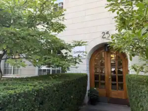 Entré till Limbra klinik med träport och gröna buskar.